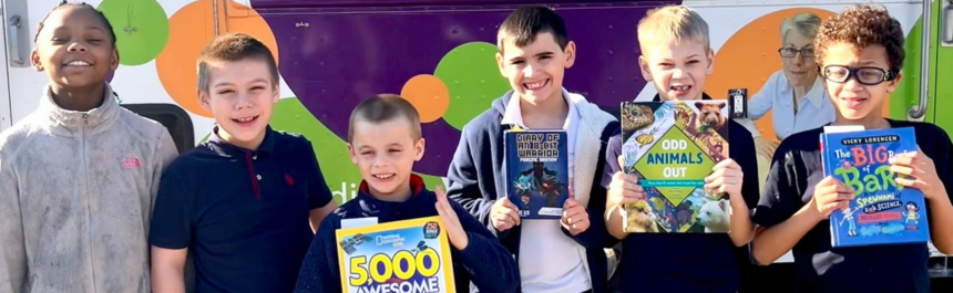 several boys stand in front of the Bookmobile. Some of the boys are holding up books