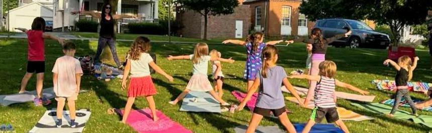 A sunny park in Newstead NY, ten children follow a yoga instructor's directions. 