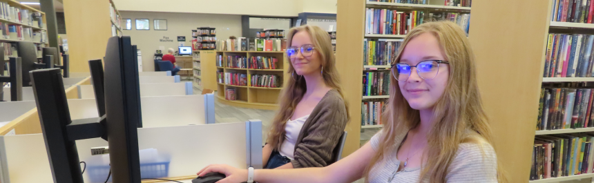 Two students sitting at computers doing homework and looking at the camera.
